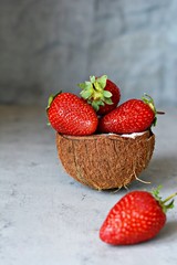 Ripe fresh strawberries in a half of coconut on a blue (gray) background. Superfood, healthy breakfast and delicious raw dessert. Healthy food concept, vegan food.