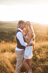 Rustic, boho and people concept. Boho woman in dress and feather accessories in the hair and handsome man in stylish clothes posing in field, hugging