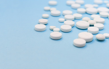 Heap of white pills, tablets, capsules on blue background. Drug prescription for treatment medication health care concept wth copy space.