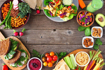 Healthy lunch food frame. Table scene with nutritious Buddha bowl, lettuce wraps, sandwiches, salad and vegetables. Overhead view over a rustic wood background. Copy space.