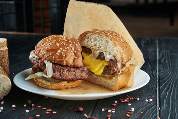 Appetizing and juicy half cuted burger with a large beef patty and cheddar cheese flowing from it, white sauce, pickled cucumber and onions on a white plate with french fries. Close up