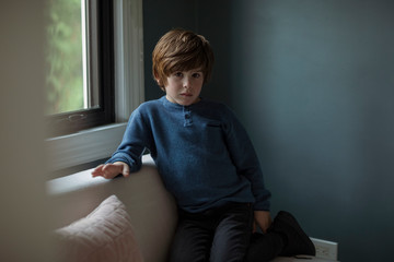 Portrait of boy kneeling on sofa against wall at home © Cavan for Adobe