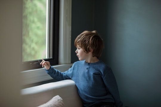 Thoughtful boy looking through window while sitting in living room at home