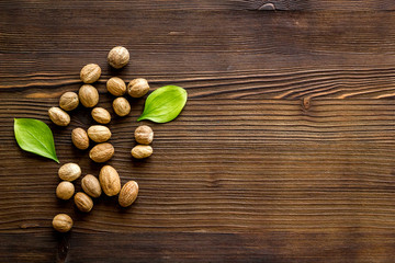 Nutmeg - whole nuts near leves - on wooden background top-down copy space