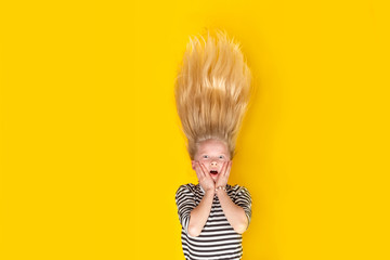 Surprised shocked little blonde girl with hair up over isolated yellow studio background. Emotion,...