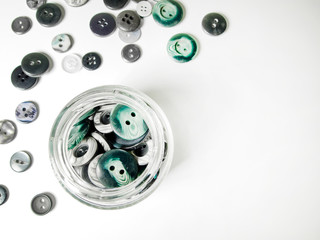 Glass jar full of clothing green, gray and black buttons on white background