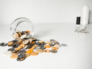 Glass jar full of clothing orange, yellow and gray buttons, thread and scissors on white background
