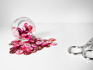Glass jar full of clothing pink buttons and scissors on white background