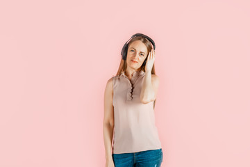 Music, leisure, hobbies. Young beautiful girl listens to music in big black headphones, pink background. Craving for art, enjoyment of creativity.