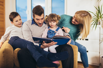 Happy family reading book at home, having fun.