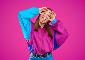 Fashion DJ girl in colorful trendy jacket from 90s. Teenager Girl shows funny face with tongue at the disco party of 80s vibes. Fashionable young model on purple color background.