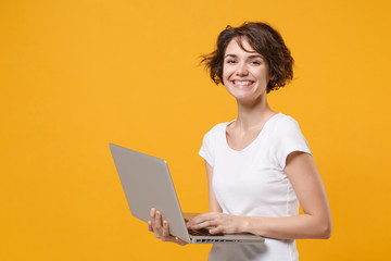 Pretty young brunette woman girl in white t-shirt posing isolated on yellow orange background studio portrait. People emotions lifestyle concept. Mock up copy space. Working on laptop pc computer.