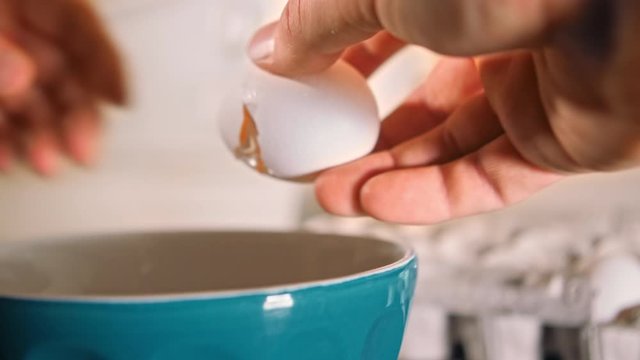 eggs cracking in bowl slow motion - male hands crack egg and pour into teal bowl in kitchen with shallow depth of field