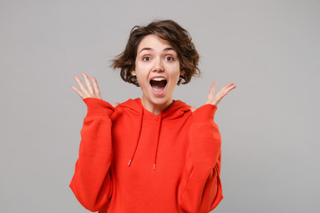 Surprised young brunette woman girl in casual red hoodie posing isolated on grey wall background...