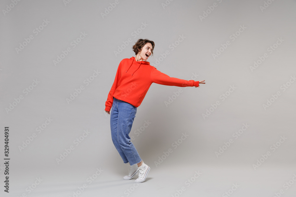 Wall mural side view of cheerful young brunette woman girl in casual red hoodie blue jeans posing isolated on g