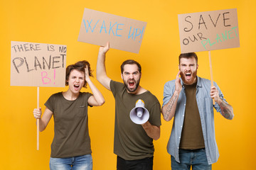 Shocked protesting young three people hold protest signs broadsheet placard scream in megaphone isolated on yellow background. Stop nature garbage ecology environment protection concept. Save planet.