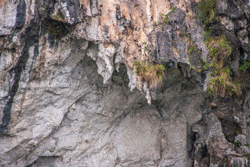 Guilin, China - May 10, 2010: Along Li River. Closeup of white, brown and black curtain rocks hide opening to cave on cliff. Green folage covers some parts.