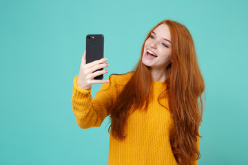Cheerful young redhead woman girl in yellow sweater posing isolated on blue turquoise wall...