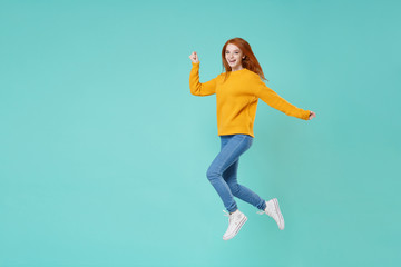 Fototapeta na wymiar Laughing young redhead woman girl in yellow knitted sweater posing isolated on blue turquoise background studio portrait. People emotions lifestyle concept. Mock up copy space. Jump spreading hands.