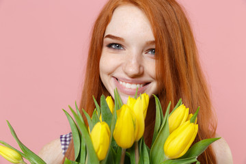 Close up of smiling young redhead woman girl in plaid dress posing isolated on pastel pink wall background studio portrait. People lifestyle concept. Mock up copy space. Hold bouquet of yellow tulips.