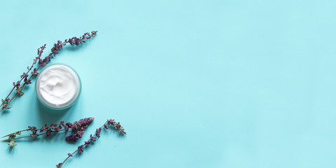 Concept of natural beauty products. With white  cream and lavender flower for skin care on a pastel blue background with green leaves. Top view and copy space Flat lay.