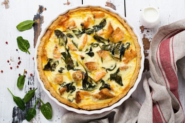 Homemade quiche tart with red fish and spinach on light wooden background. Vintage style. Top view.