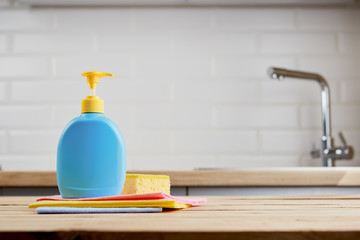 yellow sponge and bottle with hygiene liquid on wooden table with color cloths, kitchen background, close up