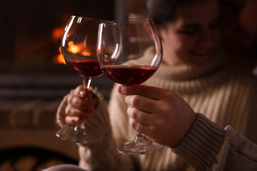 Lovely couple with glasses of wine near fireplace at home, focus on hands. Winter vacation