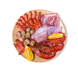 Isolated seacuterie board with raw shrimps, squid, shellfish, langoustines and lemon on light wood. White background, top view