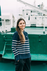 Portrait of a cute smiling caucasian girl with long hair in casual stylish clothes. Woman in a striped stylish jacket on a background of a barge.