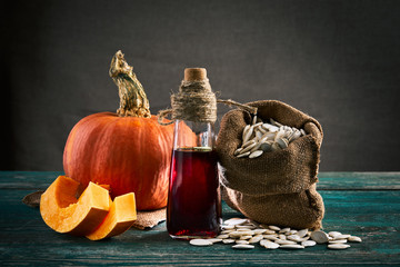Pumpkin seed oil in bottle with seeds and raw pumpkin on wooden background. Close up.