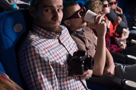 a young guy, looking around, in fear of being seen behind an illegal pirate video in a movie theater. Against the backdrop of sitting people of different sexes watching a movie in the cinema