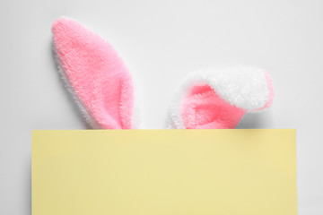 Decorative bunny ears and yellow card on white background, top view. Easter holiday
