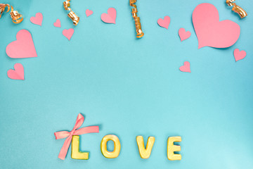 Valentines day concept. Pink paper hearts, confetti and word love on blue background. Top view, flat lay.