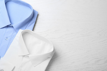 Stylish shirts on white wooden table, flat lay with space for text. Dry-cleaning service