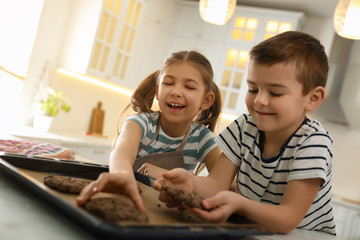Cute little children with fresh delicious cookies in kitchen. Cooking together