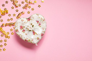 Heart shaped Valentines Day gift box on pink paper background with small stars, gold curved ribbon.