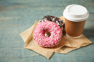 Yummy donuts with sprinkles and paper cup on wooden table