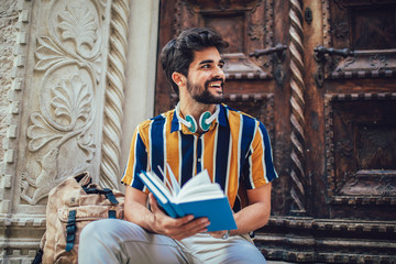 Smiling student reading a book outdoor, studying and preparing for exams at the university or college.