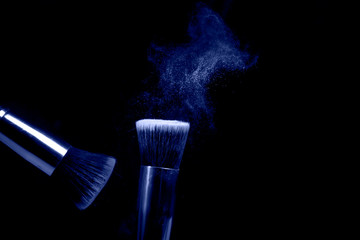 Two make up brushes with flying color powder, product on black background. Concept of glamour make up in minimal black
