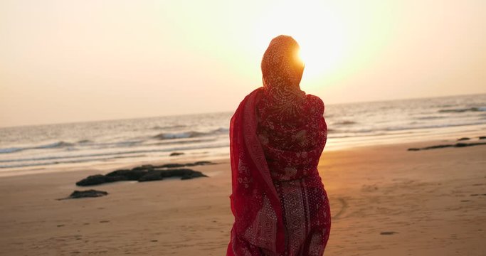 Young women wearing a red saree on the beach goa India.girl in traditional indian sari on the shore of a paradise island among the rocks and sand enjoying the freedom and the sunset