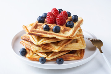 Homemade waffles with raspberries and blueberries in a plate on a white table
