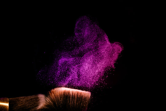 Two make up brushes with flying color powder, product on black background. Concept of glamour make up in minimal black.