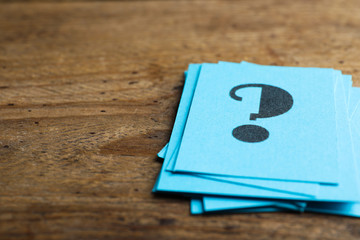 Blue paper cards with question mark on wooden background, closeup. Space for text