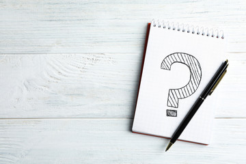 Notebook with question mark and pen on white wooden table, top view. Space for text