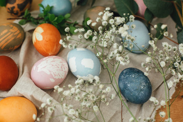 Fototapeta na wymiar Easter eggs with modern minimal ornaments painted with natural dye on rustic background. Stylish colorful Easter eggs on wooden table with spring flowers and green branches. Zero waste holiday