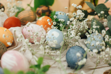 Easter eggs with modern minimal ornaments painted with natural dye on rustic background. Stylish colorful Easter eggs on wooden table with spring flowers and green branches. Zero waste holiday