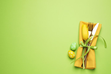 Top view of cutlery set with floral decor on green background, space for text. Easter celebration