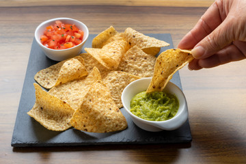 Hand taking Mexican Nachos tortillas with two sauces to eat, guacamole and chopped tomatoes with parsley