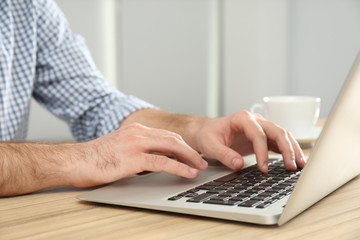 Man working with modern laptop at wooden table indoors, closeup